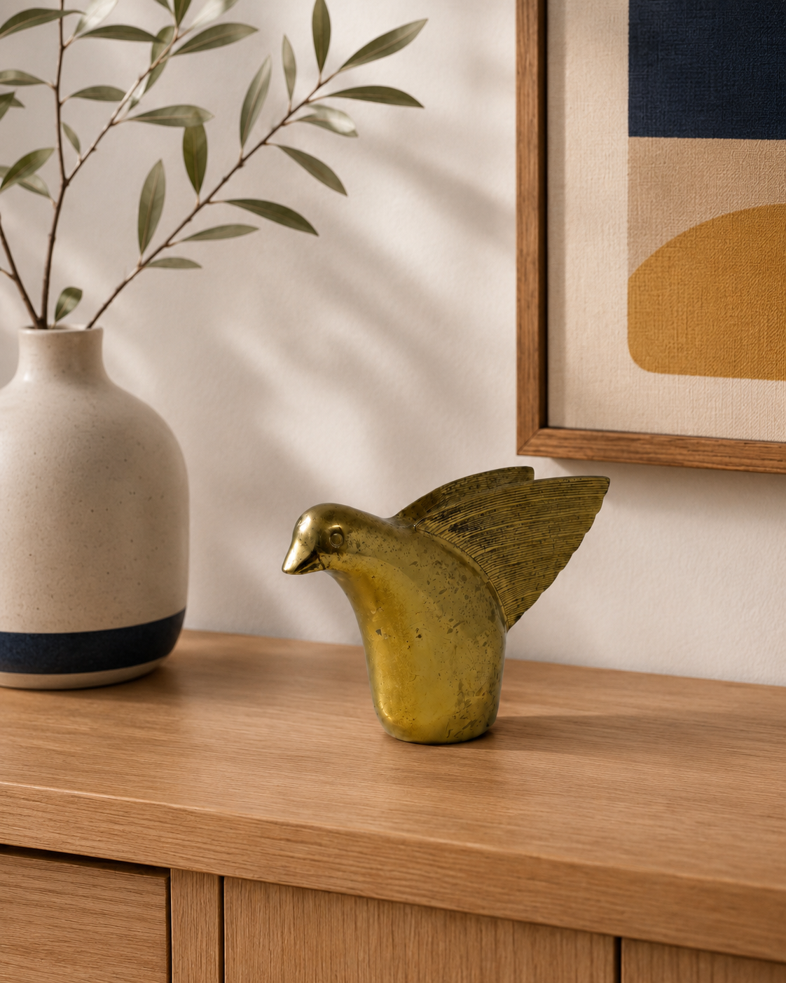 Decorative gold bird sculpture on a wooden surface with a vase and abstract art in the background.