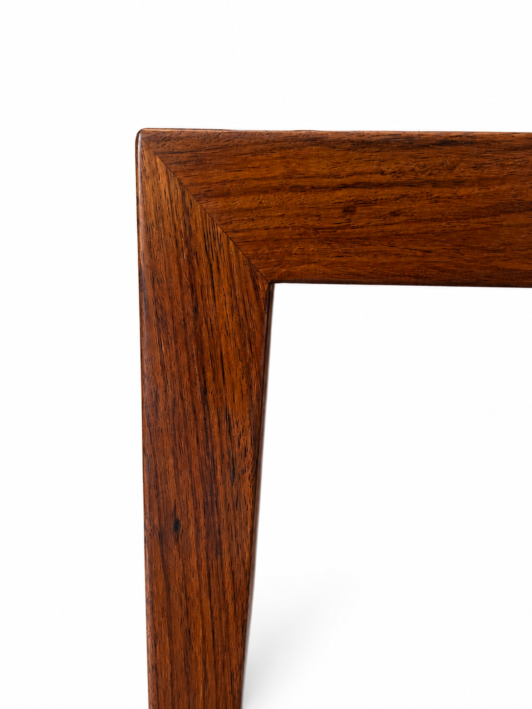 Close-up of the corner of a wooden table or frame, showing a warm medium-brown wood grain finish against a plain white background.